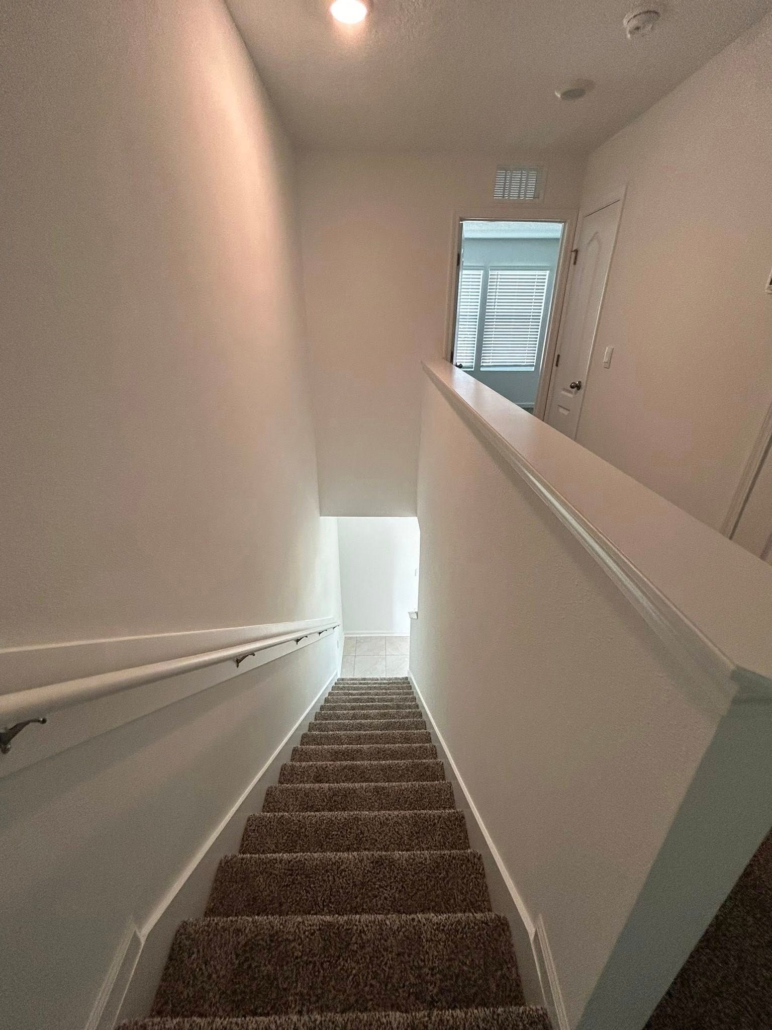 Staircase with carpeted steps and white walls. A doorway is visible at the top.