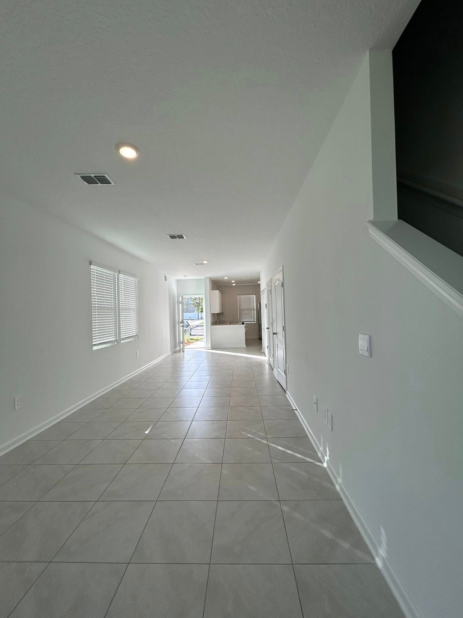 Long, bright hallway with gray tile floor, white walls and a kitchen at the end.