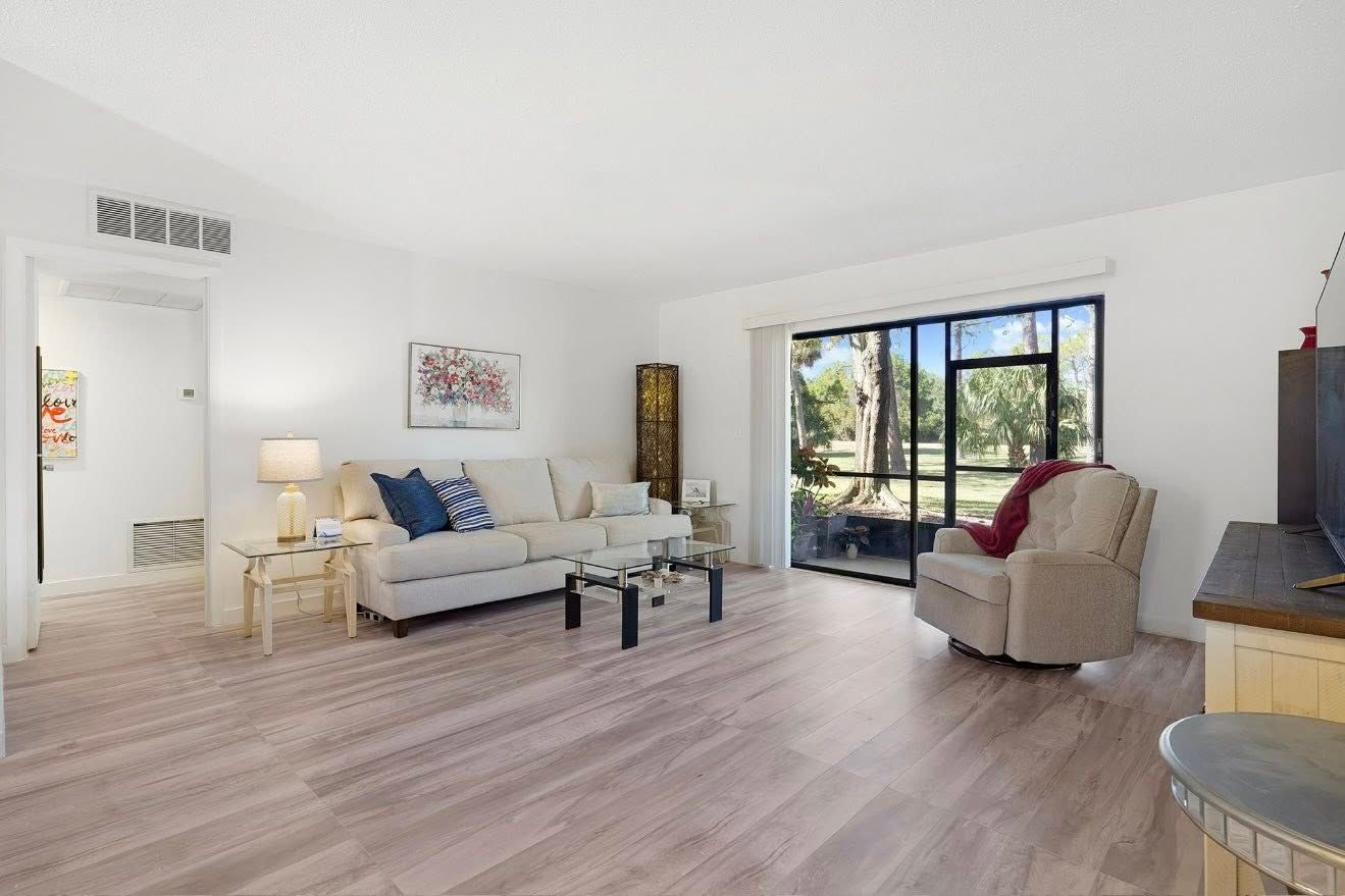 Bright living room with light wood floors, sofa, recliner, and glass doors to a view.