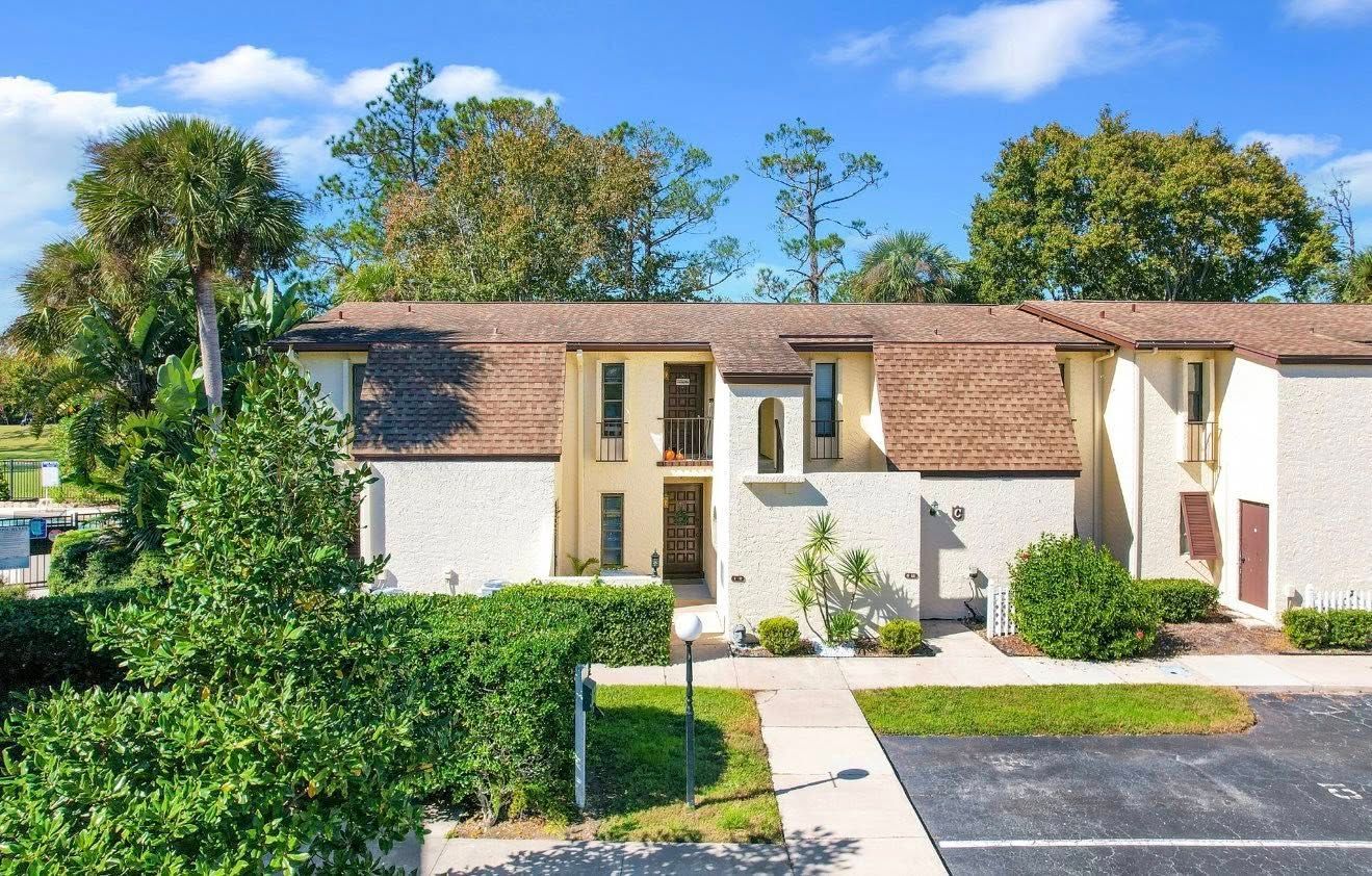 Townhouse complex with light stucco exterior, brown roof, and green landscaping.