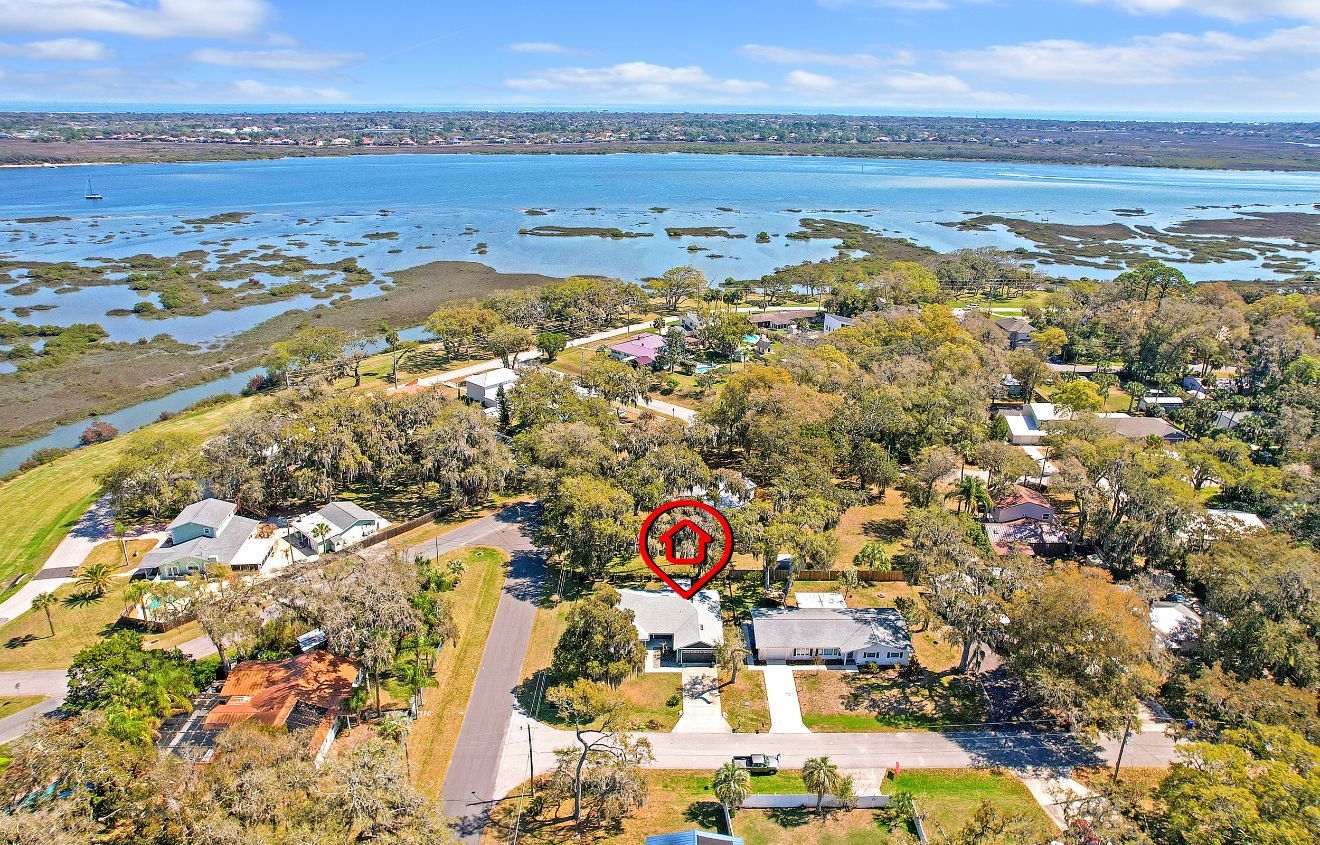 Aerial view of a coastal residential neighborhood with a red location pin highlighting a specific house near the water.
