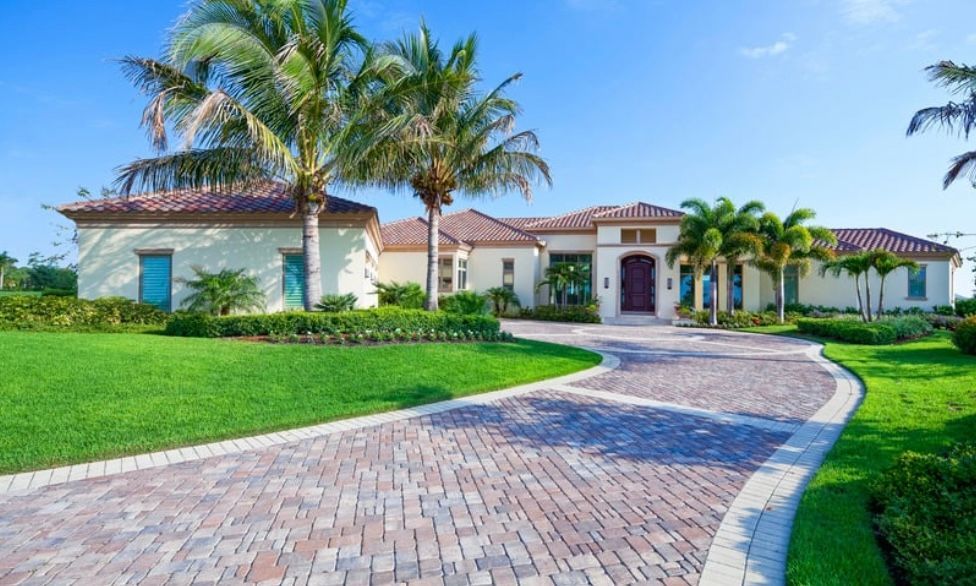 Luxury single-story house with palm trees, a curved brick driveway, and a manicured green lawn