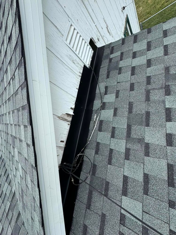 View of a dark metal valley where two roofs meet. The left roof has shingles, and the right has a downspout.