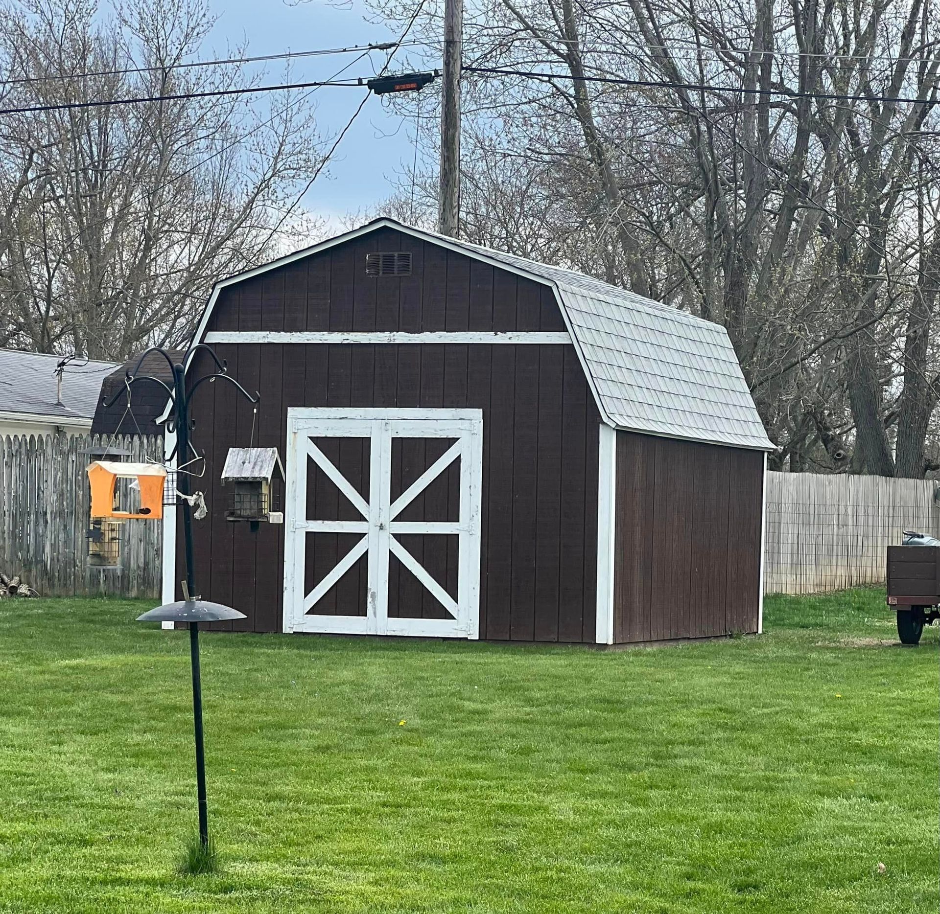Brown barn with white trim and doors in a grassy yard, with bird feeders in front.