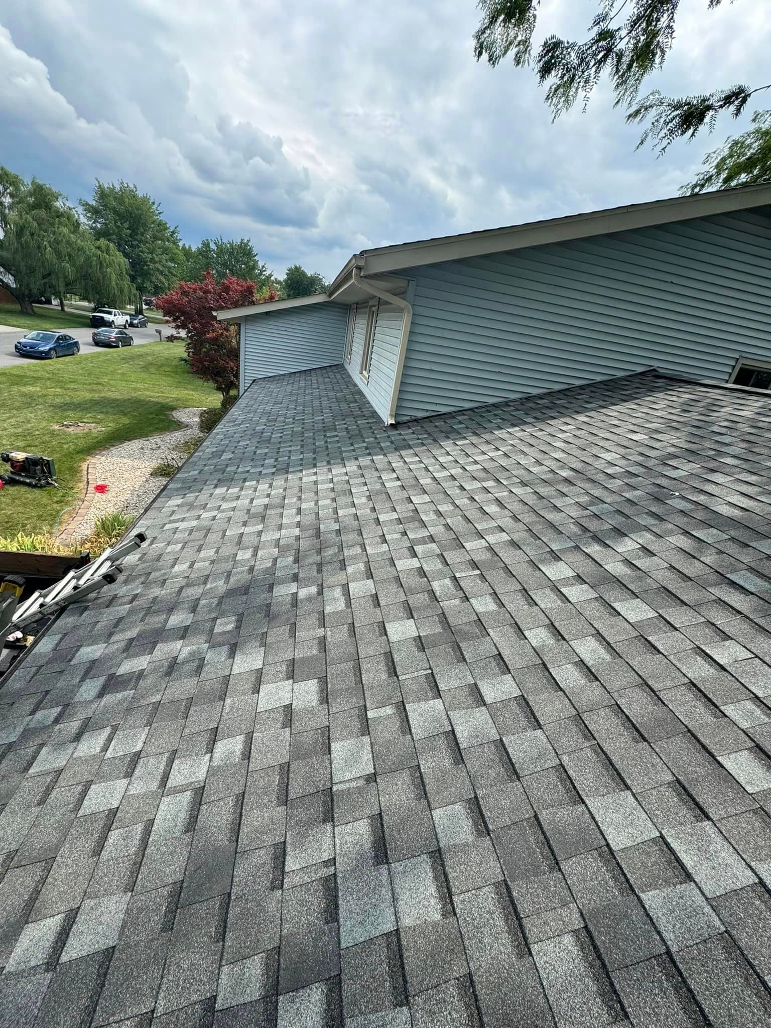 Roof covered in gray shingles against a light blue siding and cloudy sky.