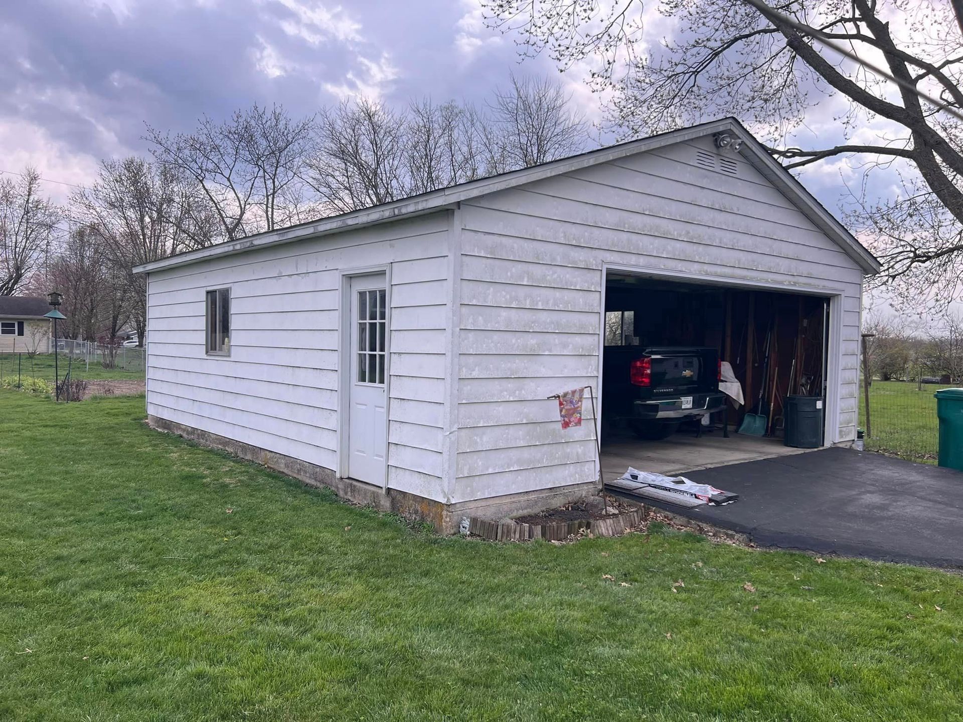 White garage with open door, car inside, green grass, cloudy sky.