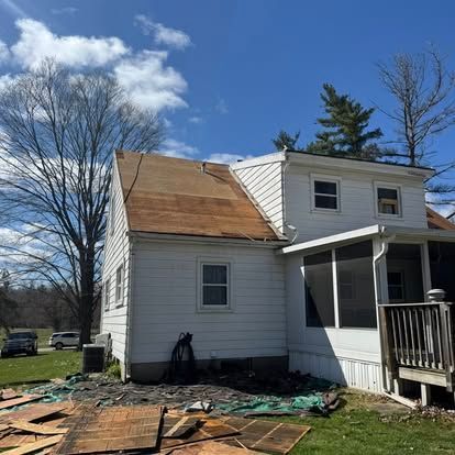 White house with roof partially torn off, debris on the ground. Blue sky.