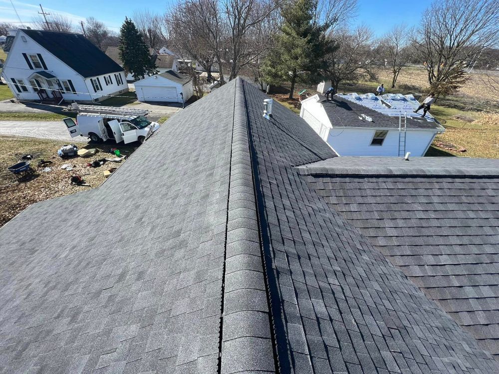 Gray shingle roof being installed with workers on adjacent white house roof.