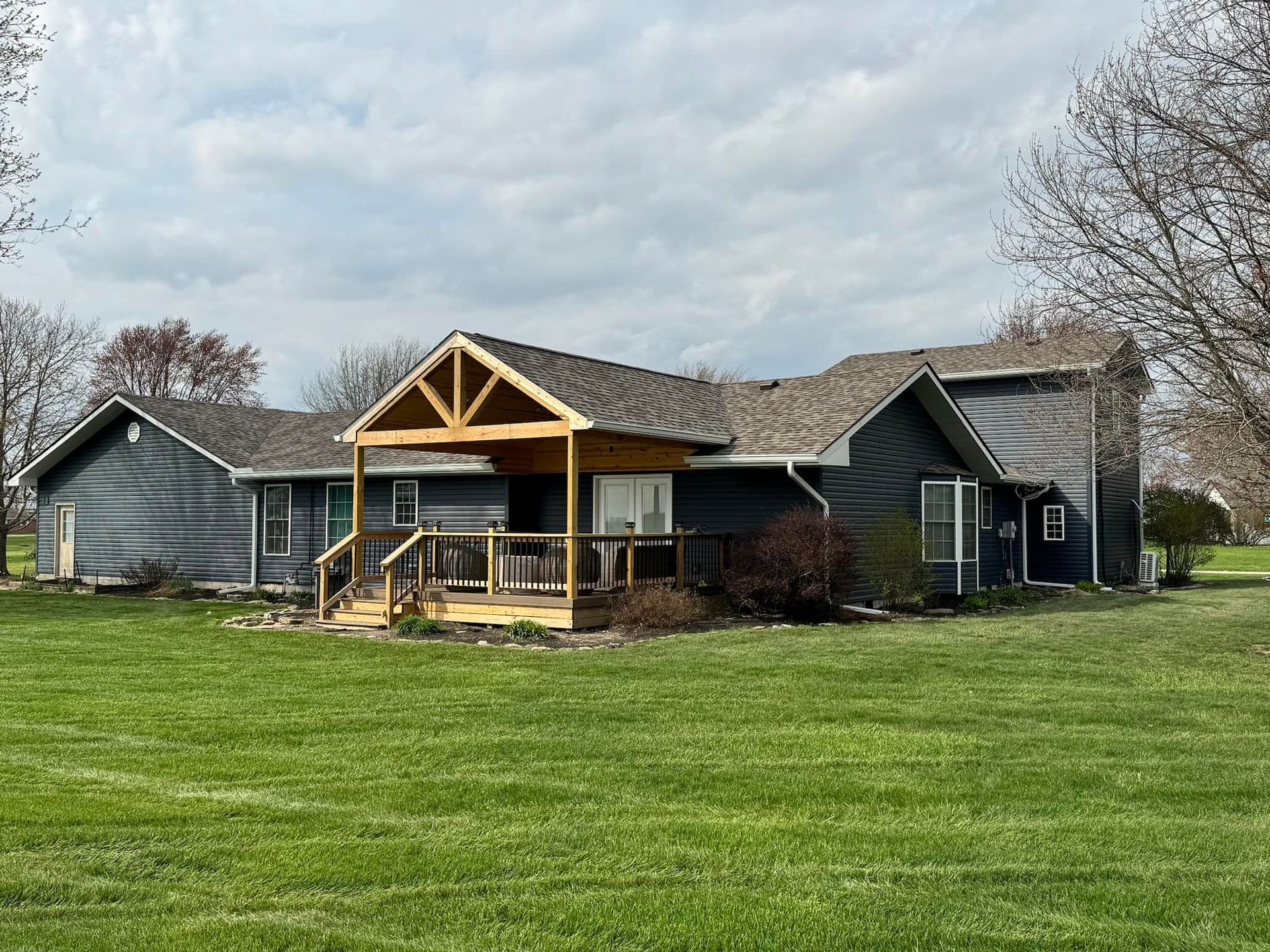 Dark blue house with a wooden porch, set on a green lawn under a cloudy sky.