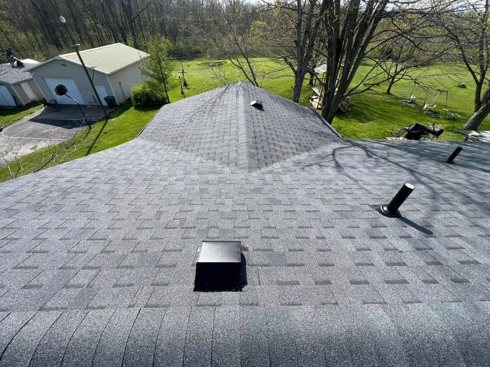 A gray asphalt shingle roof with vents and a chimney in a residential area.