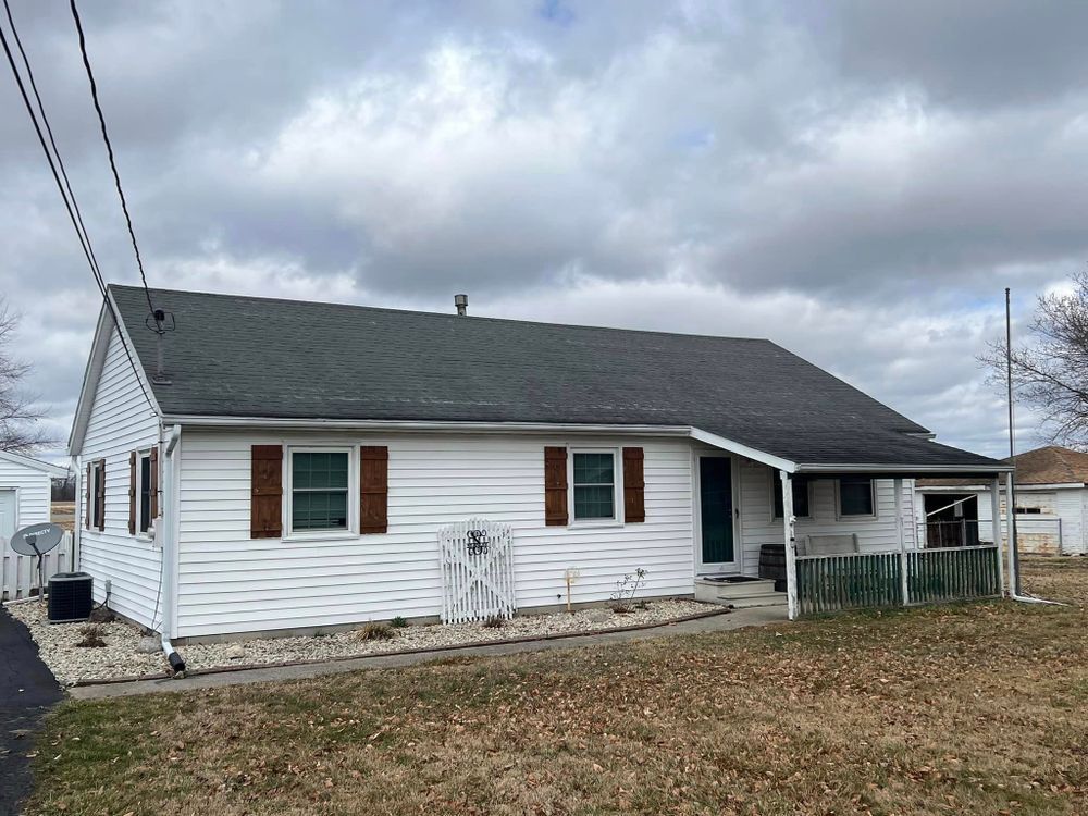White house with dark roof and brown shutters under cloudy sky.