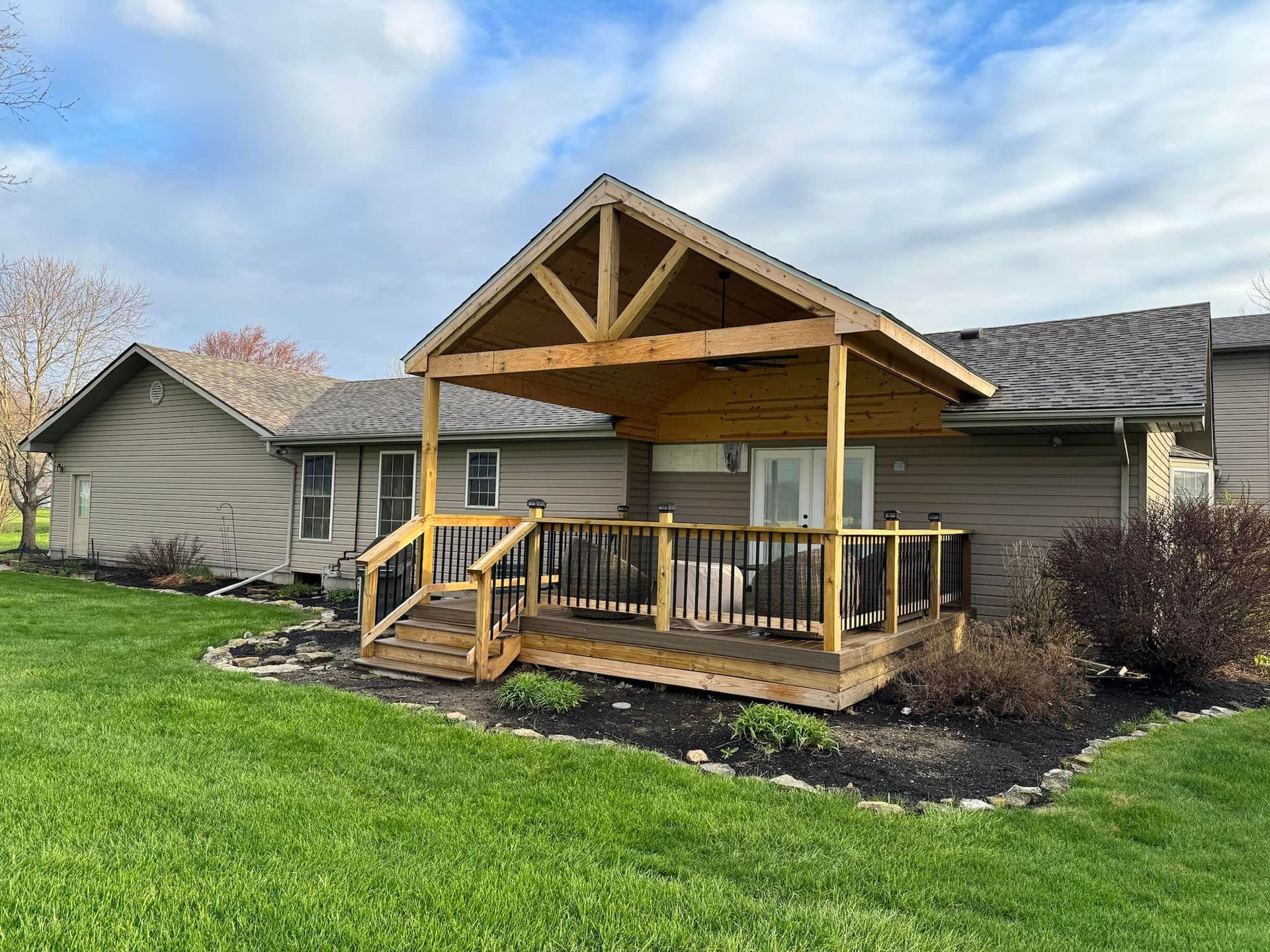 Wooden deck with a covered porch and black railing. The house is beige.