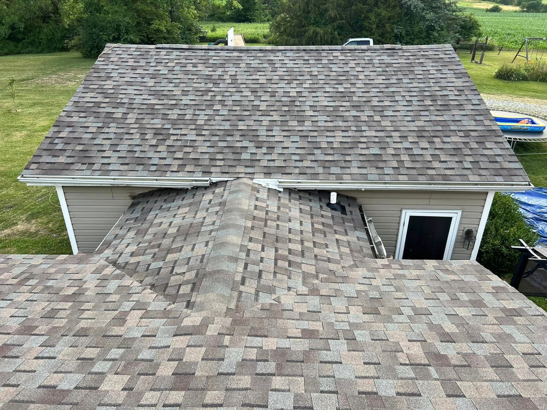 Overhead view of a house with a grey shingled roof, green grass, and a clear sky.