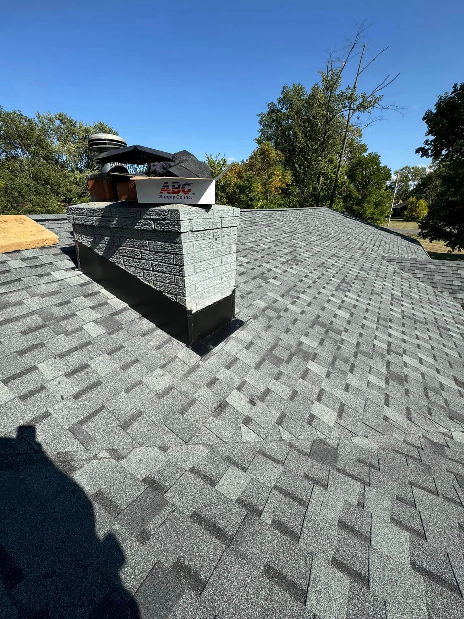 Roof with a chimney, covered in gray shingles, under a clear blue sky.