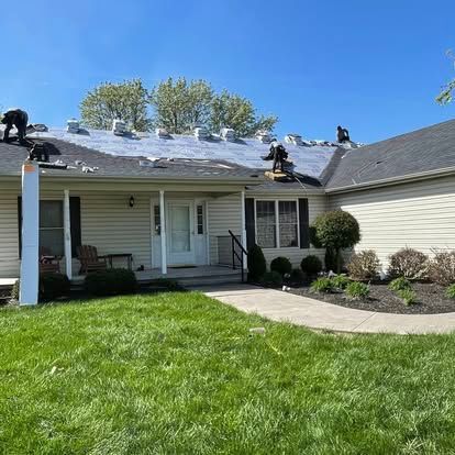 Roofers working on a house, removing old shingles on a sunny day.