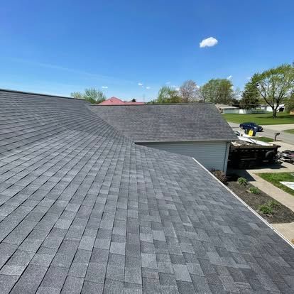 Gray shingled roofs under a bright blue sky with a few trees and a suburban street.
