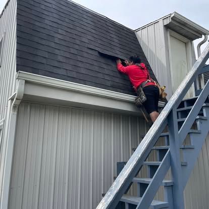 Person in red shirt repairs roof on a building with stairs.