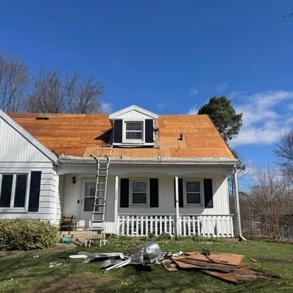 House with exposed roof during renovation; ladder, debris on lawn, blue sky.