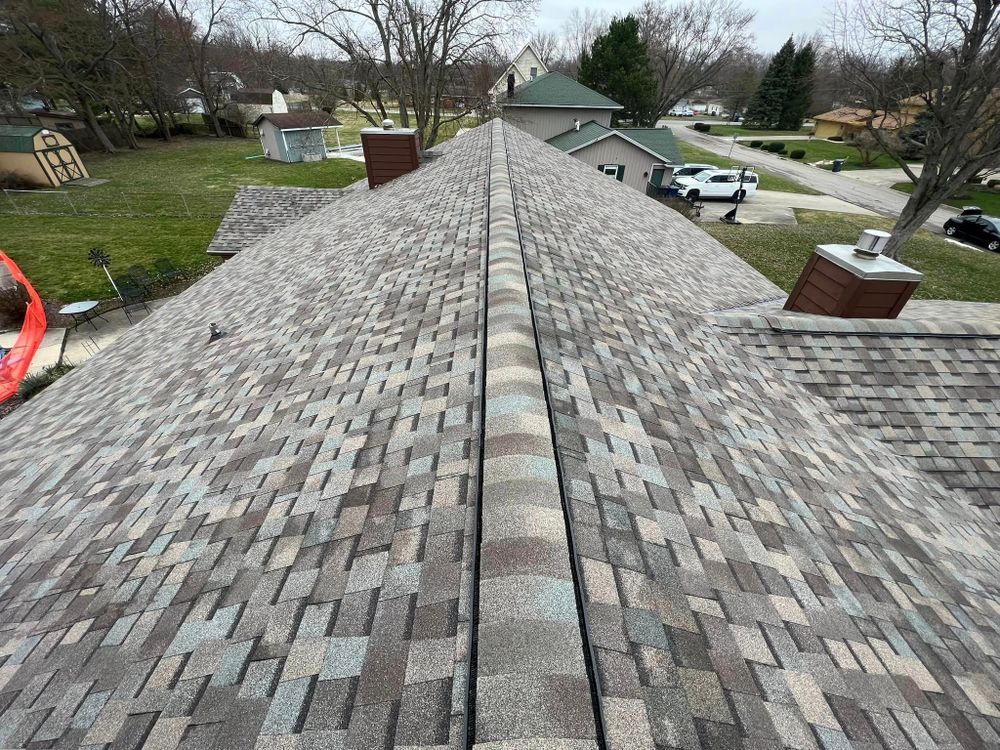 View of a multi-colored shingle roof with a central ridge and chimneys, in a suburban setting.