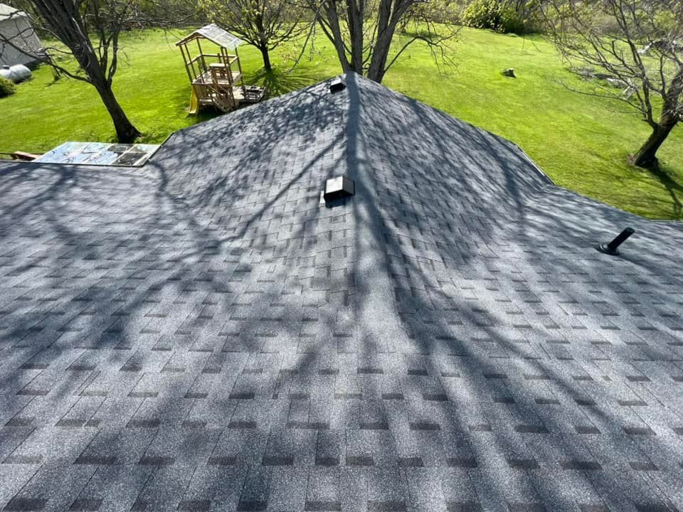 Gray asphalt shingle roof with a grassy background and trees casting shadows.