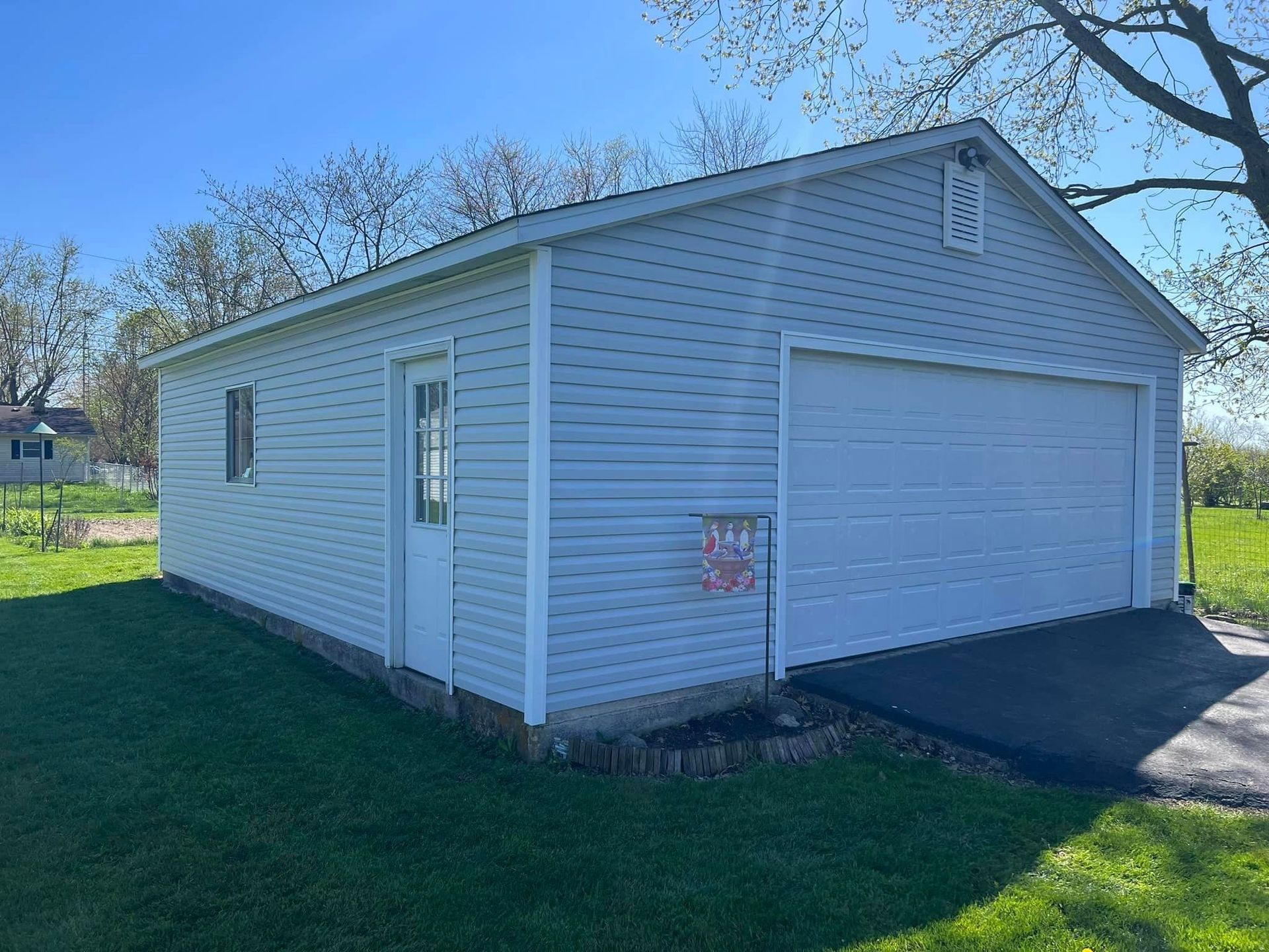 A light blue garage with a white door and a closed garage door on green grass under a blue sky.