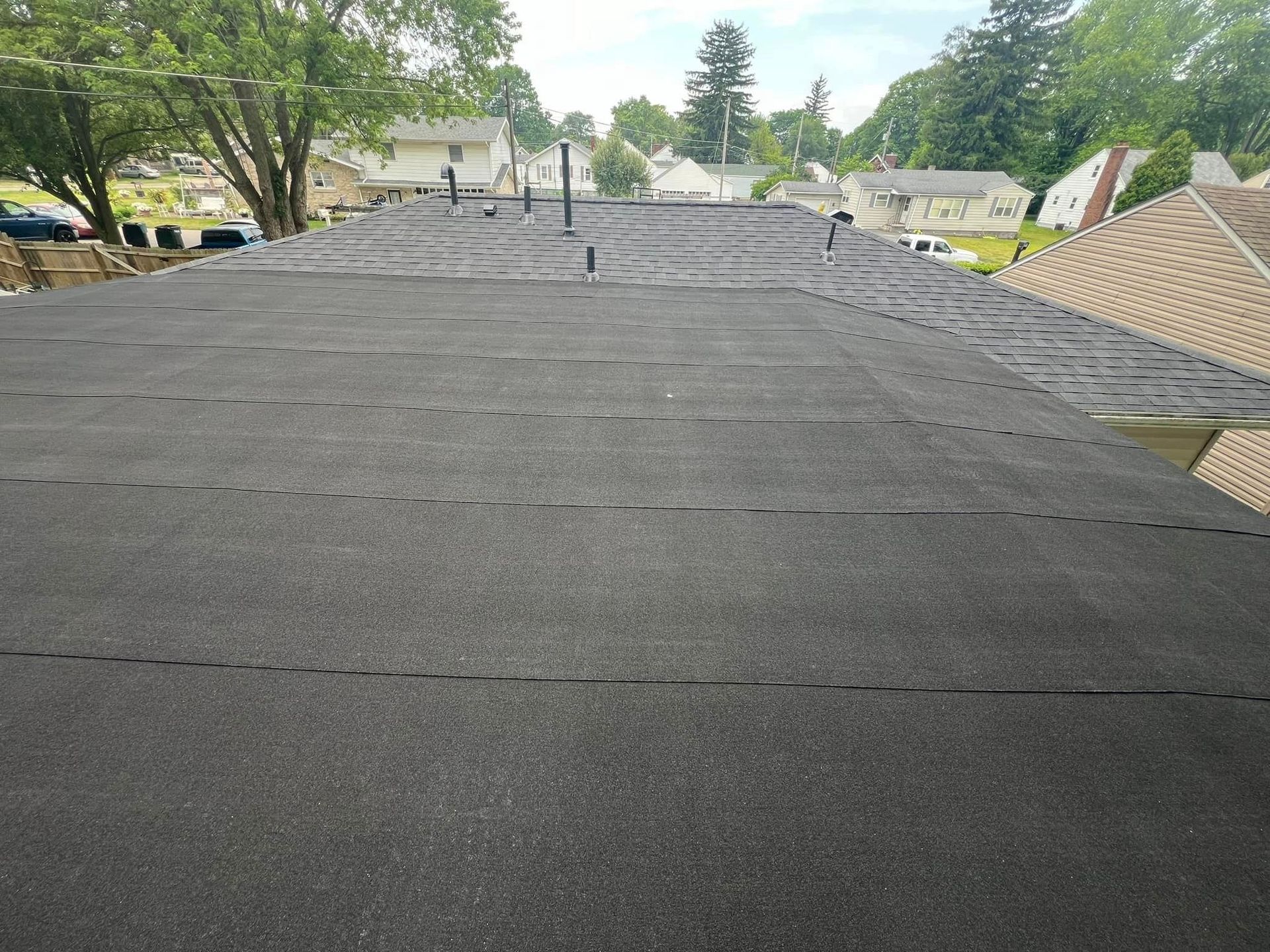 Flat black roof with various pipes extending upward; suburban setting.
