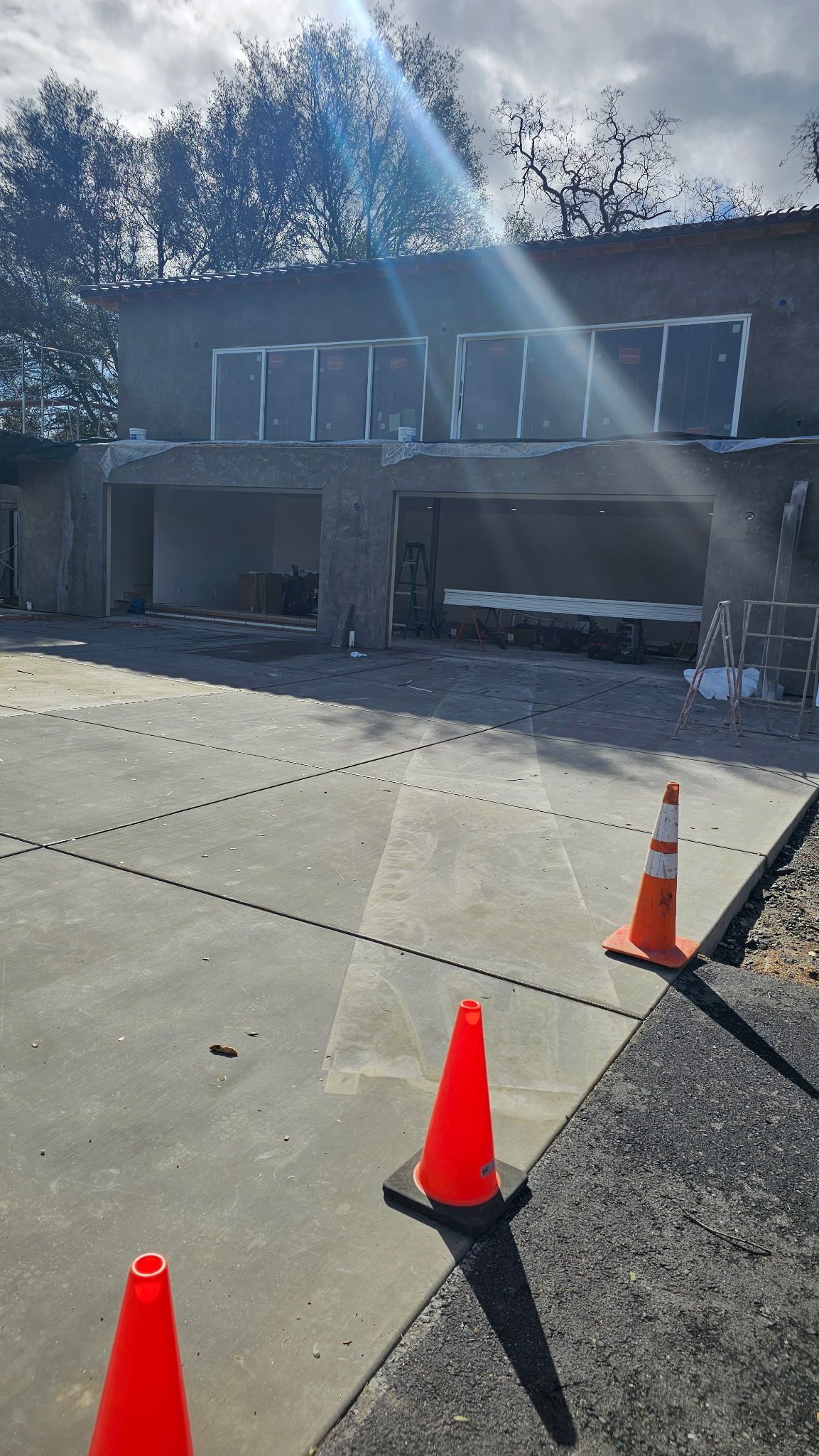 Two orange traffic cones are sitting on the sidewalk in front of a building under construction.