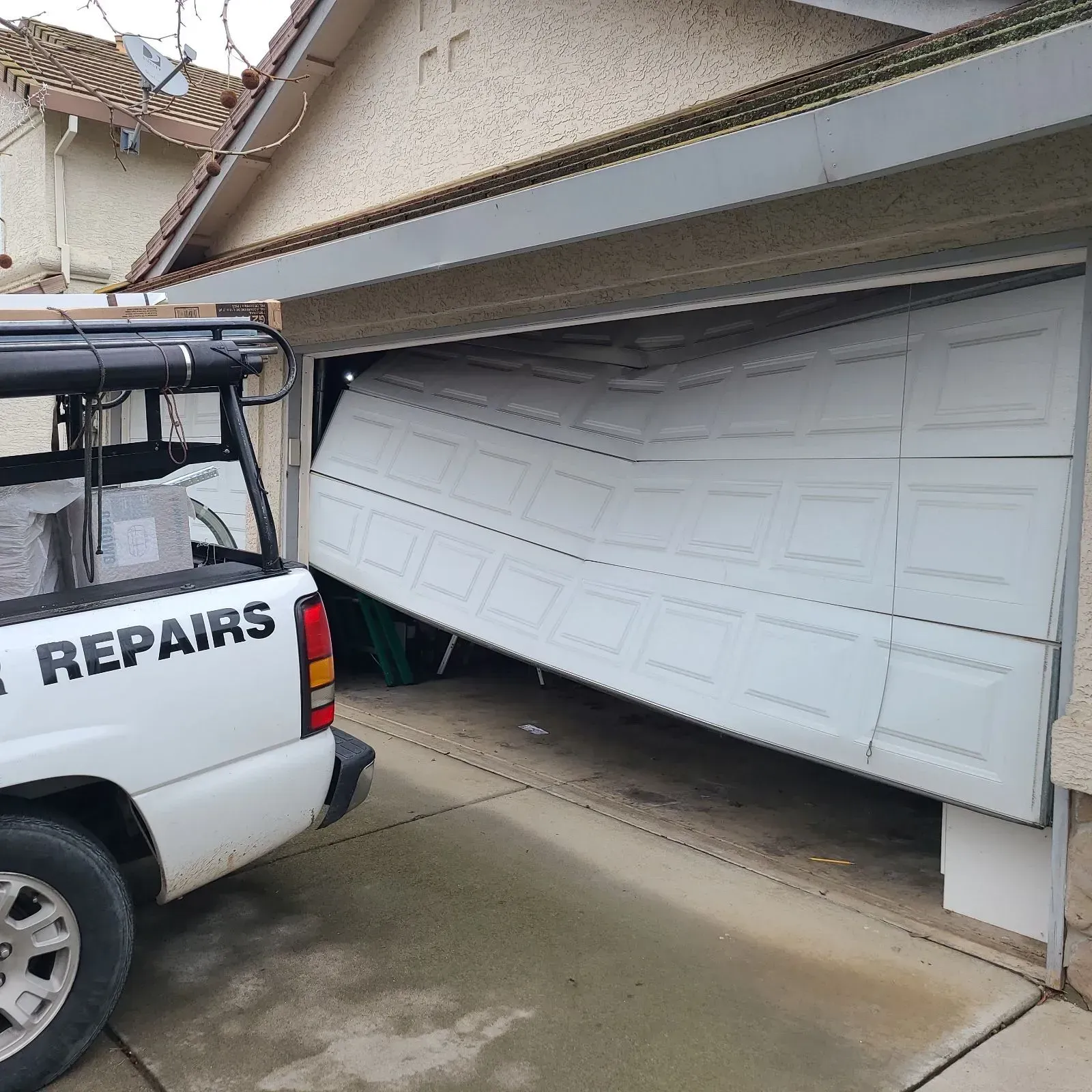 White garage door bent outward next to a repair truck in a driveway