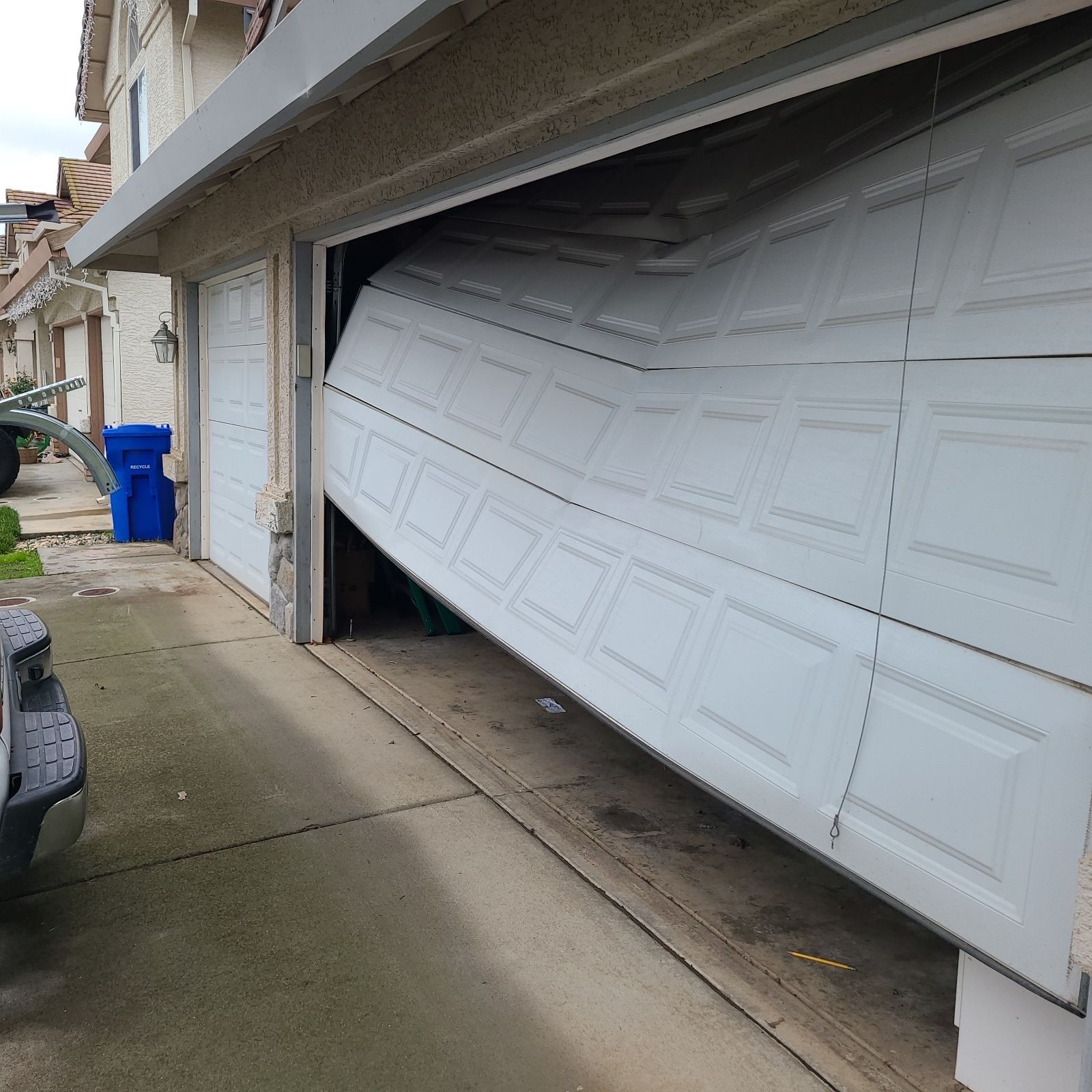 A broken garage door is sitting on the sidewalk in front of a house.