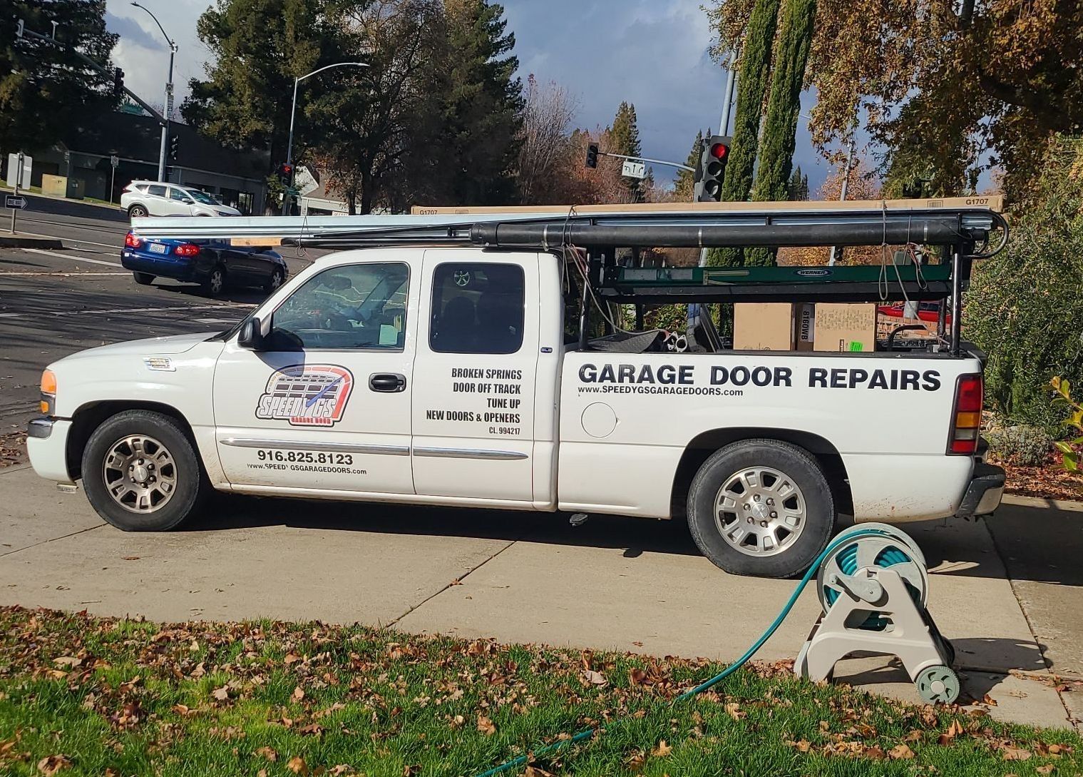 A white garage door repair truck is parked on the side of the road.