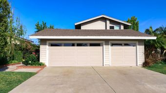 Suburban two-story house with a white garage and driveway under a blue sky