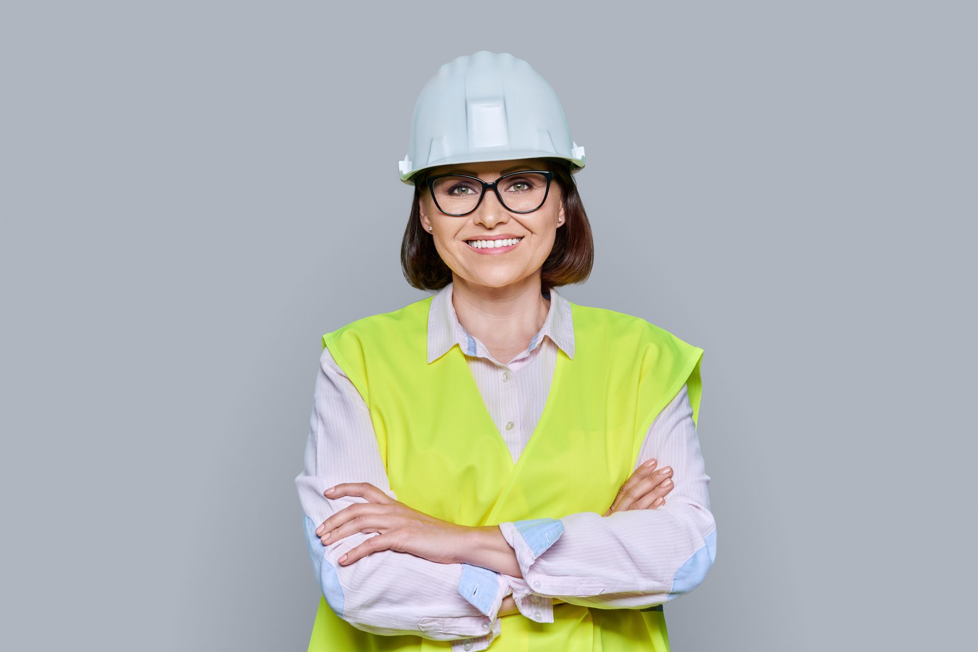 Woman in safety vest and hard hat smiles with arms crossed.