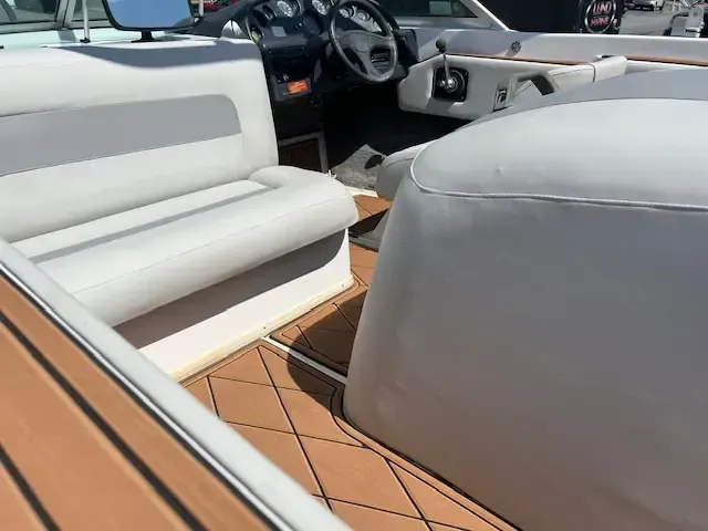 Interior view of a boat with white seating, a steering wheel, and brown flooring with black diamond stitching.