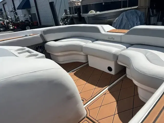 Interior of a boat with white and gray cushioned seating, tan flooring, and cup holders.