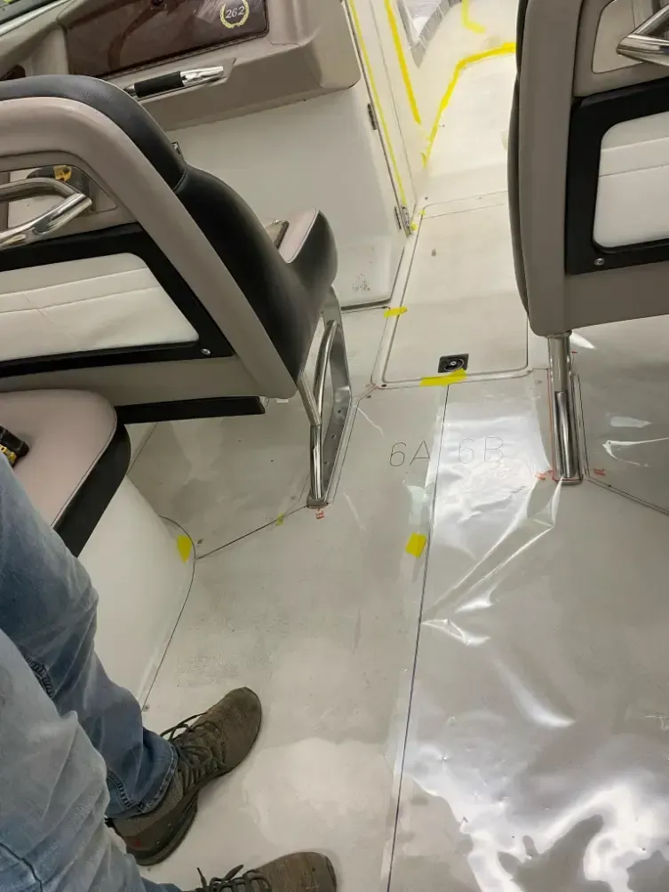 Interior view of a boat, showing two seats, white flooring, and a person's legs and feet.