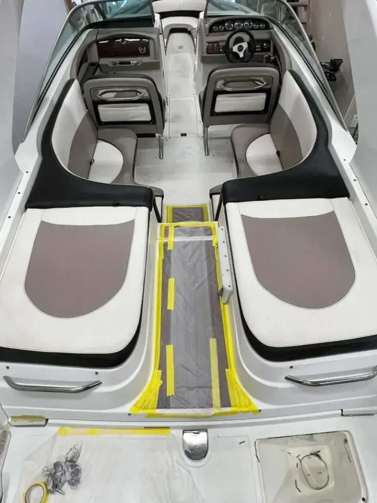 Boat interior with two rows of seats, gray, white, and black upholstery, yellow tape on floor.