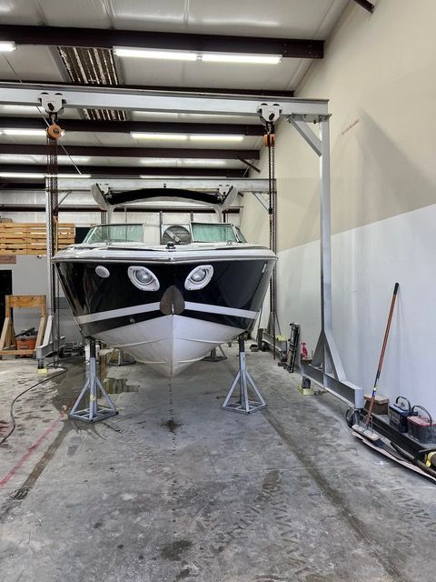 Boat inside a building being worked on. Supported by stands and hoist, white and black.