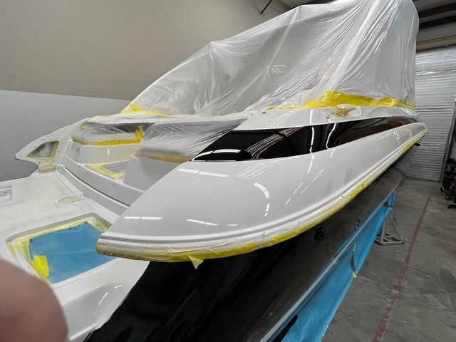 White boat hull partially covered in plastic sheeting, masking tape visible, in a workshop.