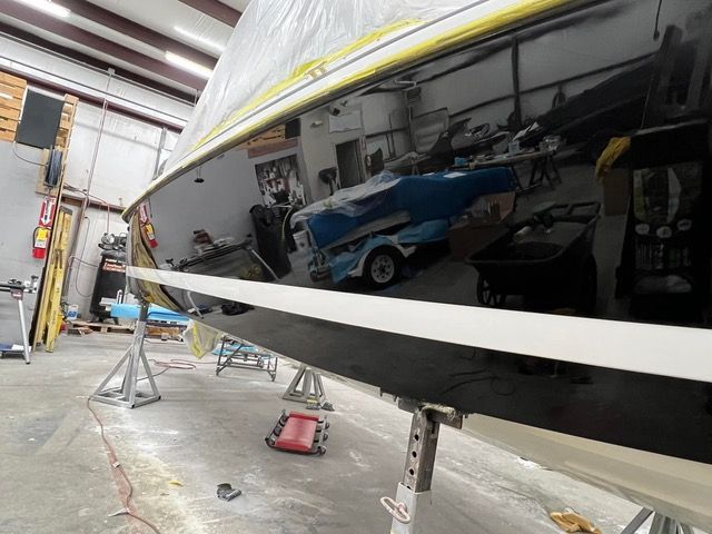 Black boat hull reflecting workshop, supported by jacks.