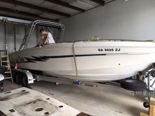 Boat on a trailer inside a garage, a person works on the boat's top.