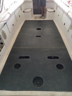 Boat deck with black flooring, various holes, and a person standing in the background.