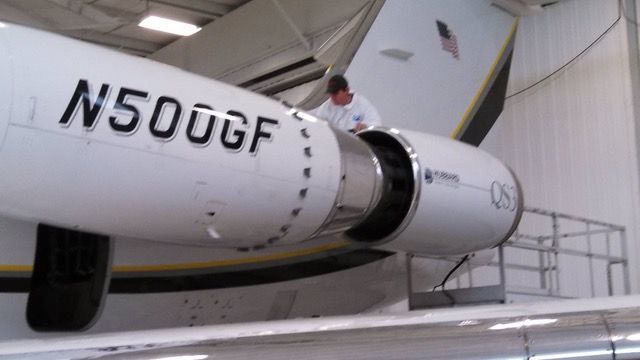 Mechanic working on the engine of a white private jet in a hangar.