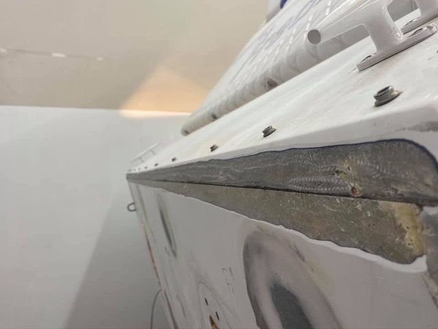 Close-up of a white boat's side, showing damaged gray edging along the hull and visible fasteners.