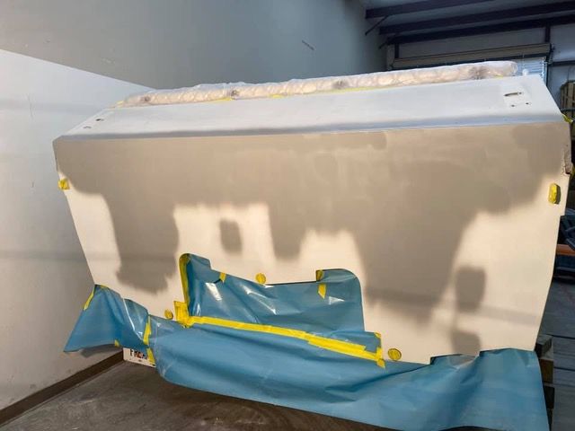 Boat stern being prepped for painting, covered in primer and masking tape in a workshop setting.