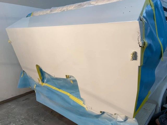 Car body panel, primed white, in a garage, taped and covered in blue, ready for painting.