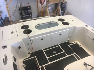 Boat interior with white compartments, black floor matting, and drink holders.