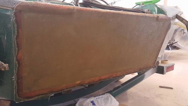 Back of a green boat on a trailer, with a brown panel and orange trim.