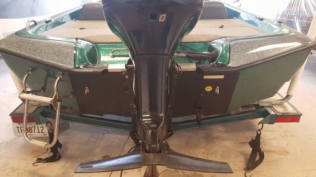 Green fishing boat with black motor on a trailer.