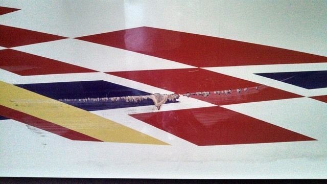 Damage on a red, white, blue, and yellow diamond-patterned surface.