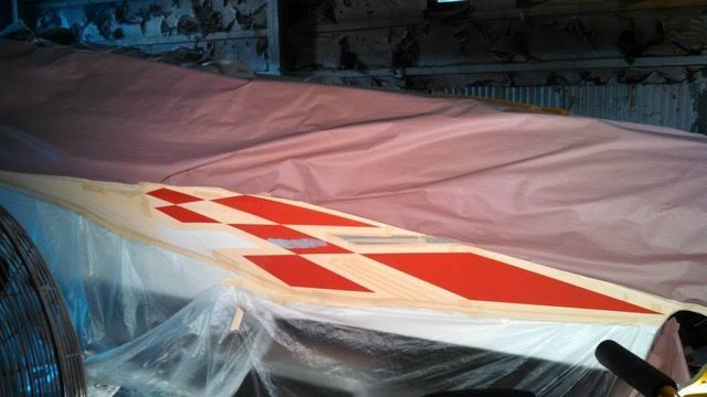 Wing of a plane being painted, with red and white geometric designs.